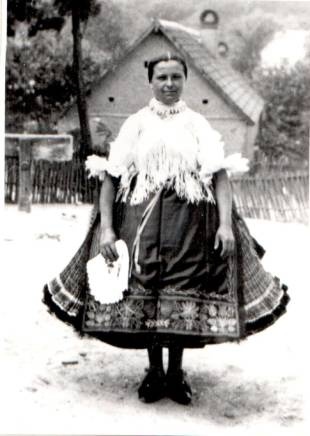 Régi, fekete-fehér felvétel. Népviseletbe öltözött nő áll a képen. A szoknyája, a sok réteg miatt feltűnően bő.
