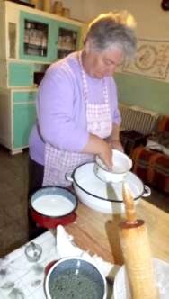 Egy konyh�ban az alapanyagokat k�sz�ti el� egy k�t�nyt visel� asszony. El�tte asztal, ed�nyek, ny�jt�fa. 