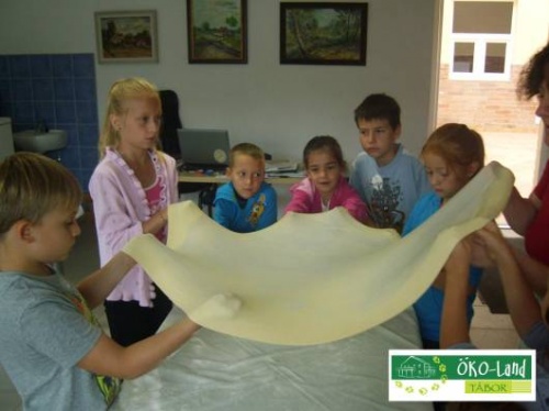 7 gyerek k�rben �ll egy szob�ban. A kez�kben v�konyra ny�jtott t�szt�t fognak, mely �gy m�r nagyj�b�l 1 m sz�les lehet.